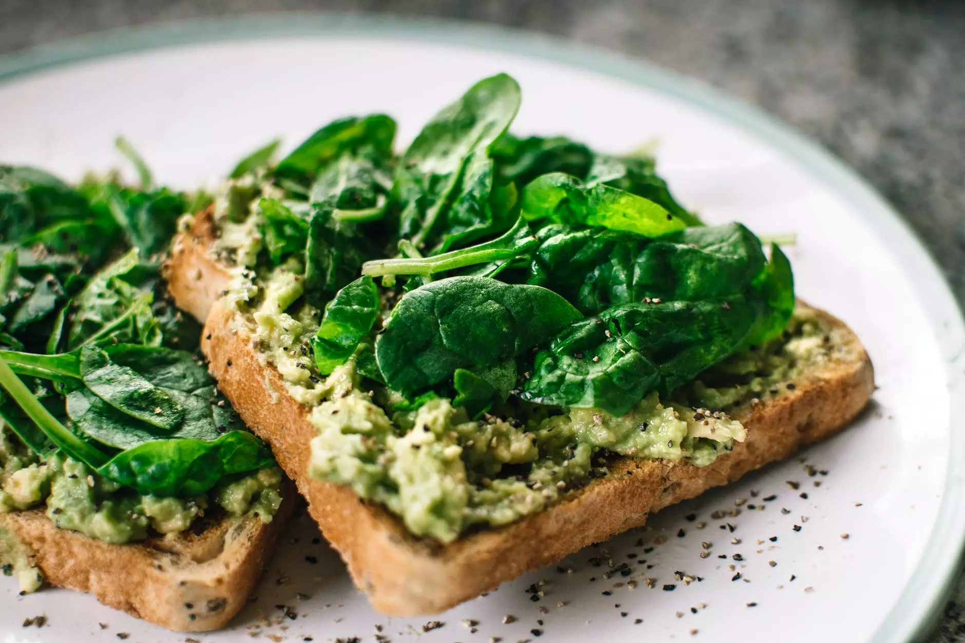 basilicumblaadjes en avocado op gesneden brood op witte keramische plaat