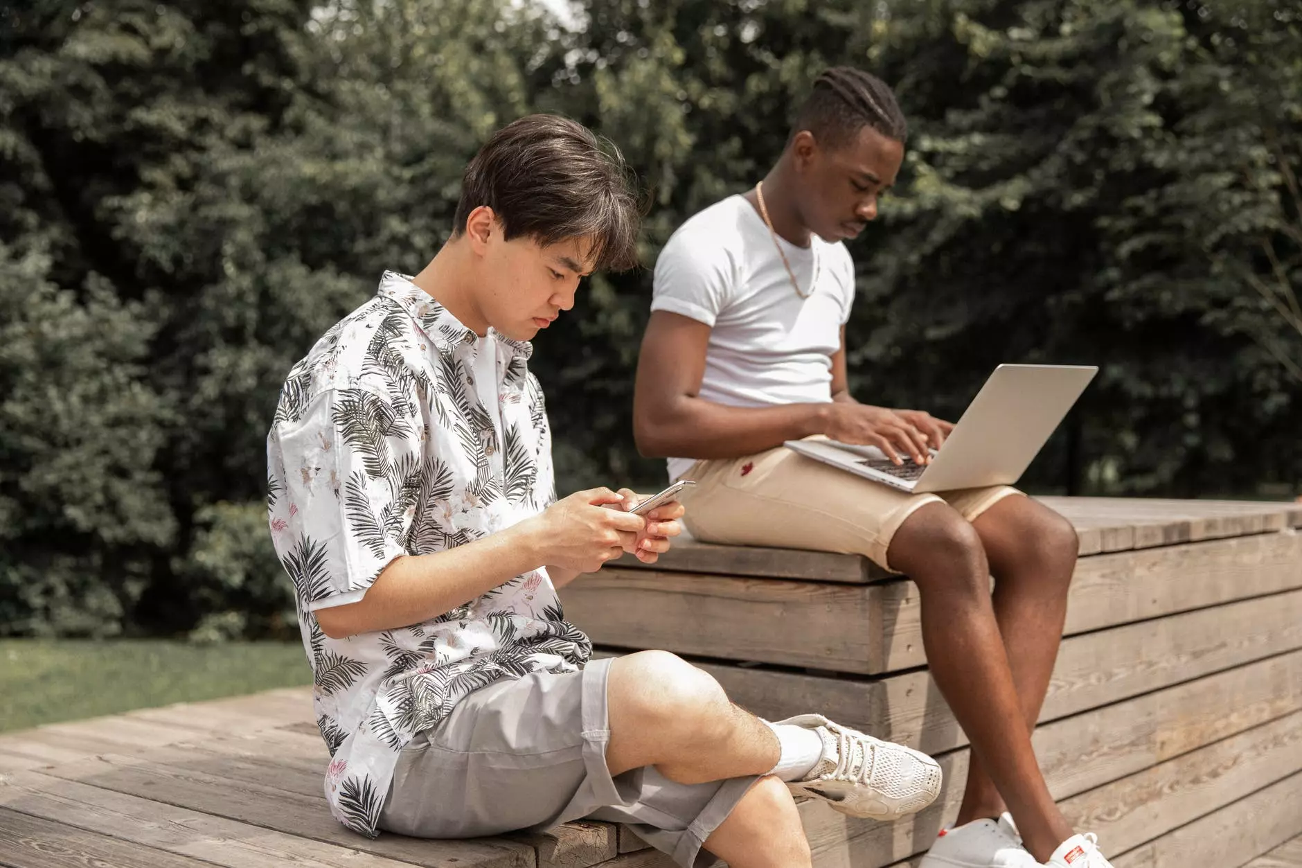 Jeunes hommes divers et occupés parcourant un ordinateur portable et un smartphone dans un parc verdoyant Photo de Gabby K sur Pexels.com