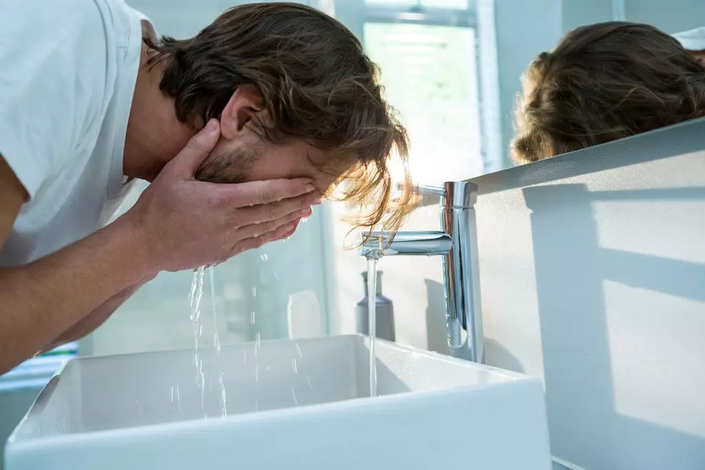 Principais formas de nutrir a túa pel propensa ao acne. Home lavando a cara con auga no baño da casa