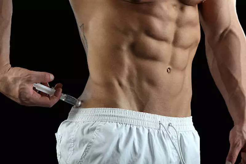 Traitement hormonal substitutif pour les hommes. Bodybuilder prenant l'injection de stéroïdes en bout isolé sur fond noir