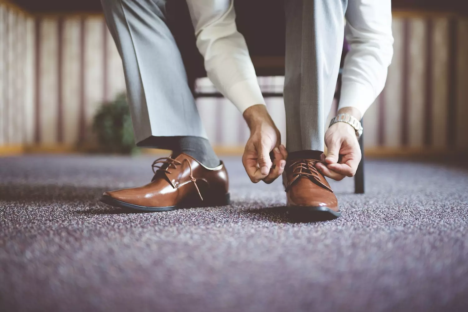 4 zeitlose Styling-Tipps für Männer, damit sich Ihre Anwesenheit auf der Uhr anfühlt. Nahaufnahme eines Mannes, der seine Schuhe bindet und sich auf ein Geschäftstreffen vorbereitet