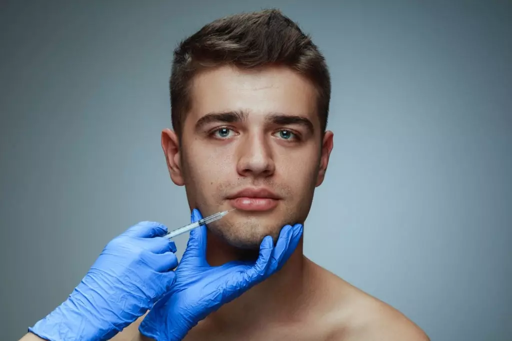 Nahaufnahmeporträt des jungen Mannes lokalisiert auf grauem Studiohintergrund. Füllung Botox-Operationsverfahren. Konzept der Männergesundheit und -schönheit, Kosmetik, Selbstpflege, Körper- und Hautpflege. Antialterung.